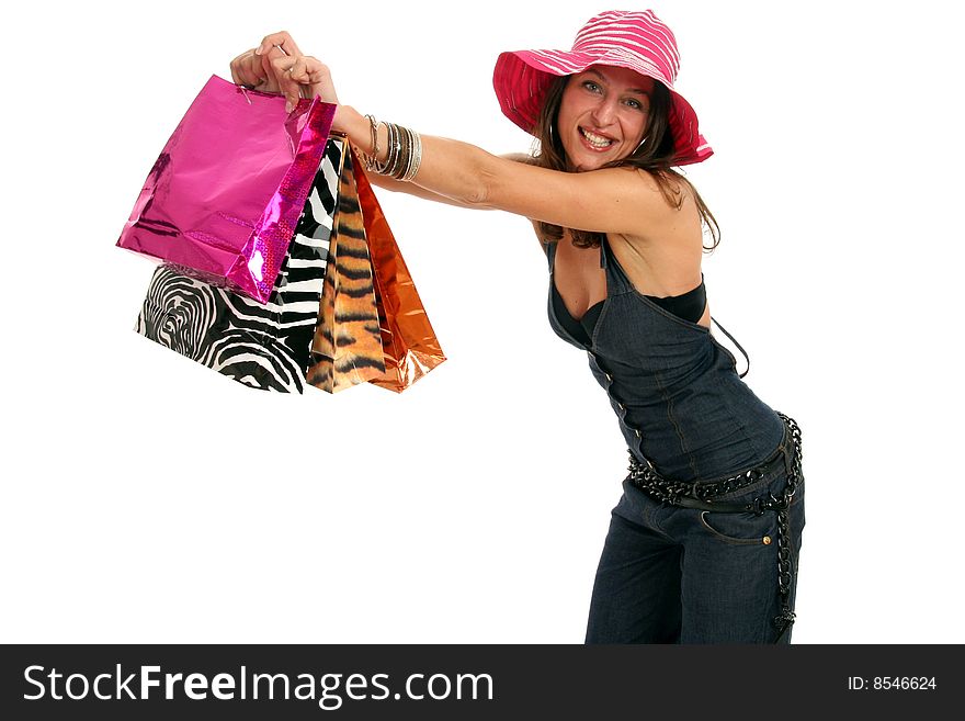 Attractive young woman making shopping and showing her colorful shopping bags, she wears jeans dress and a funny big pink hat, isolated on white. Attractive young woman making shopping and showing her colorful shopping bags, she wears jeans dress and a funny big pink hat, isolated on white