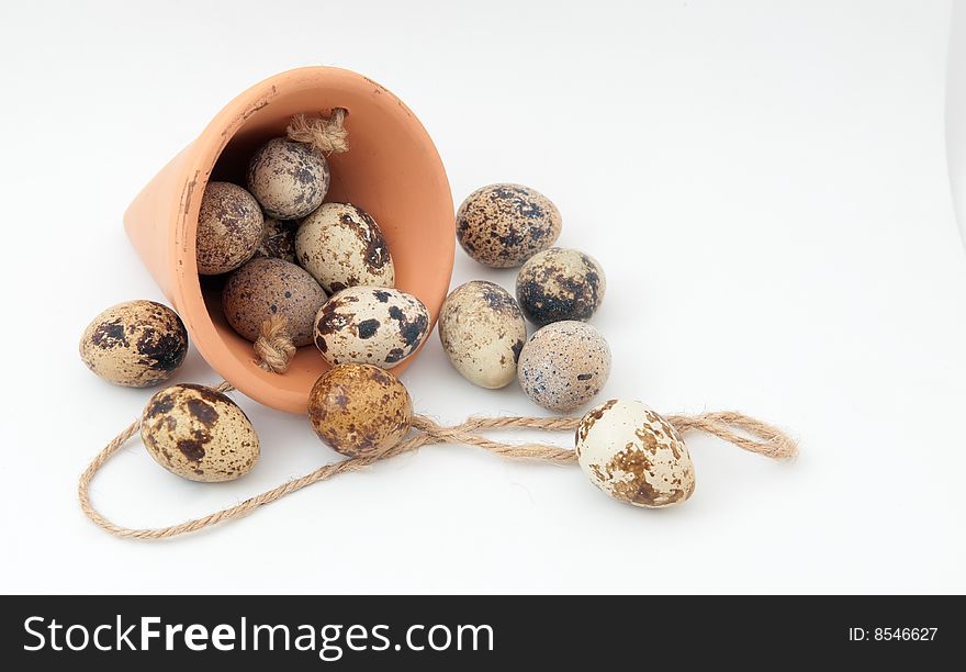 Clay conical carrier with rope overflowing with quail eggs on white background. Clay conical carrier with rope overflowing with quail eggs on white background