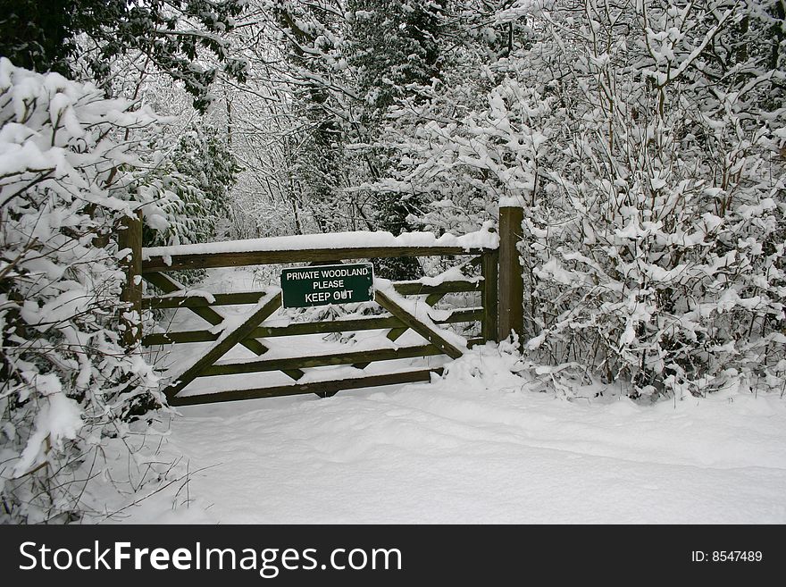 A keep out sign on a wooden gate that leads to a private woodland in winter