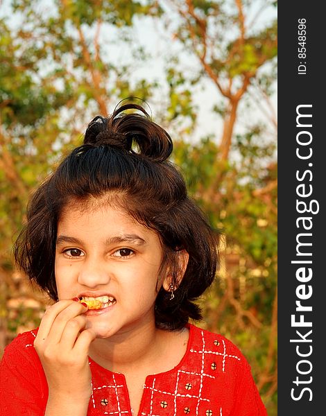 A nice and beautiful Indian girl taking a bite of her snacks.