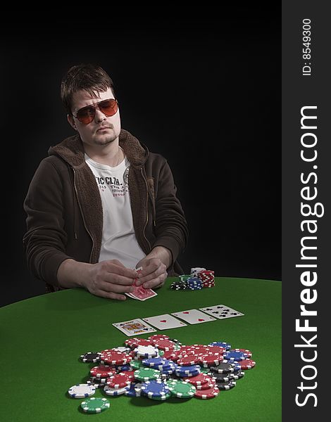 Man with sun glasses playing poker on green table. Chips and cards on the table. Man with sun glasses playing poker on green table. Chips and cards on the table.