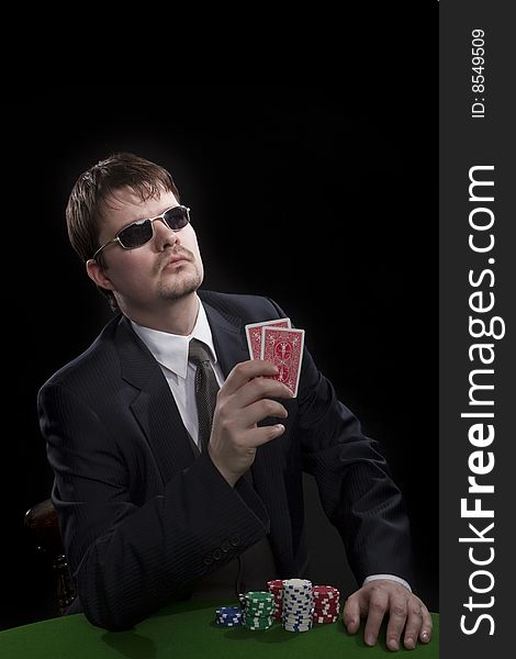 Man in suit with sun glasses playing poker on green table. Chips and cards on the table. Man in suit with sun glasses playing poker on green table. Chips and cards on the table.