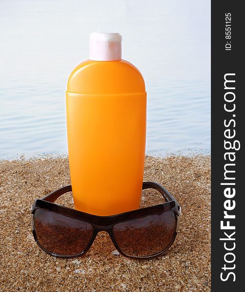 Antisun cream and antisun glasses on marine sand and on a background water