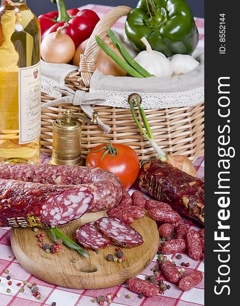 Salami sausage on a wooden plate with a background of a basket full of vegetables