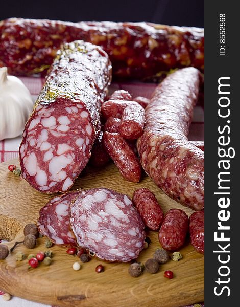 Salami sausage on a wooden plate with a background of a basket full of vegetables