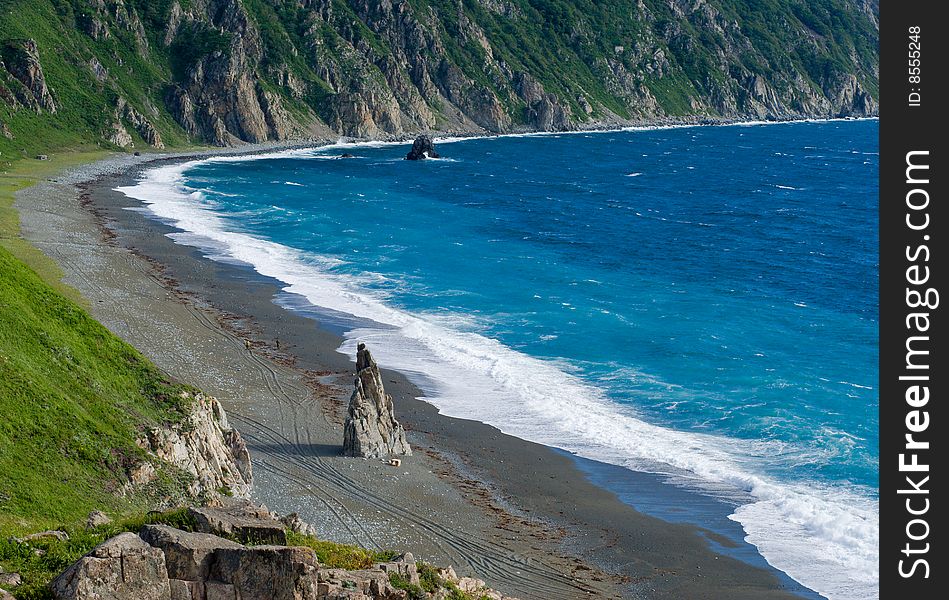 A grey beach with alone rock and white surf. . A grey beach with alone rock and white surf.