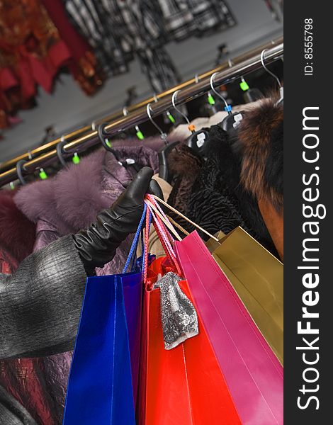 Hand holding a bunch of shopping bags in front of a clothes stall in a shop. A piece of cloth hangs out of one of the shopping bags. Hand holding a bunch of shopping bags in front of a clothes stall in a shop. A piece of cloth hangs out of one of the shopping bags.