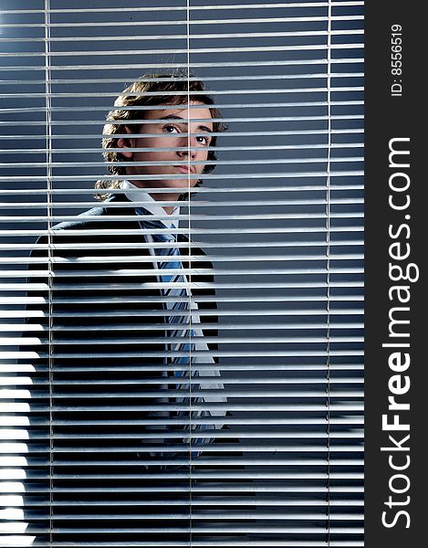 Young businessman behind a window blinds looking up. Young businessman behind a window blinds looking up