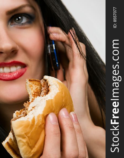 Attractive young lady eating burger, holding mobile phone. Attractive young lady eating burger, holding mobile phone