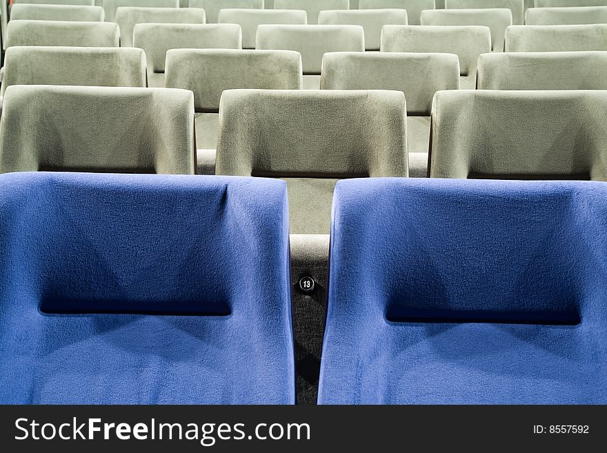 Seat number thirteen. Row of gray and blue chairs in auditorium. Seat number thirteen. Row of gray and blue chairs in auditorium.