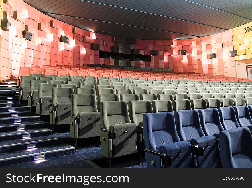 Empty new cinema auditorium with rows of blue, gray and red chairs and illuminated stairs. Empty new cinema auditorium with rows of blue, gray and red chairs and illuminated stairs.