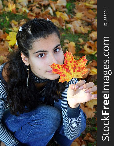 A girl sitting with the maple leaf in her hand. A girl sitting with the maple leaf in her hand