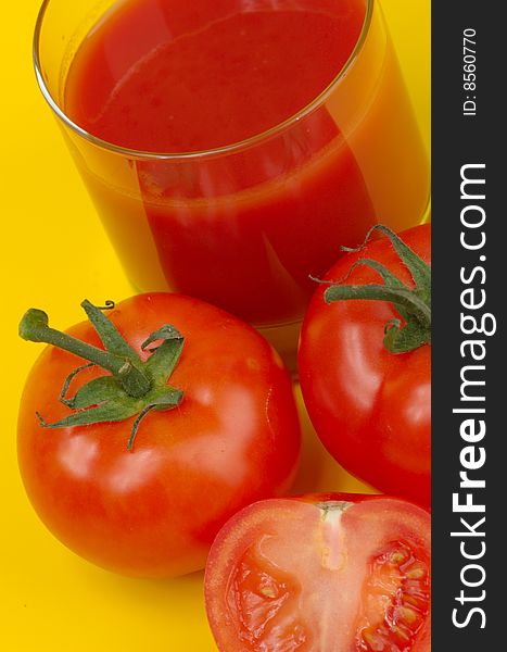 Ripe juicy tomatoes and glass of tomato juice on a yellow background. Ripe juicy tomatoes and glass of tomato juice on a yellow background