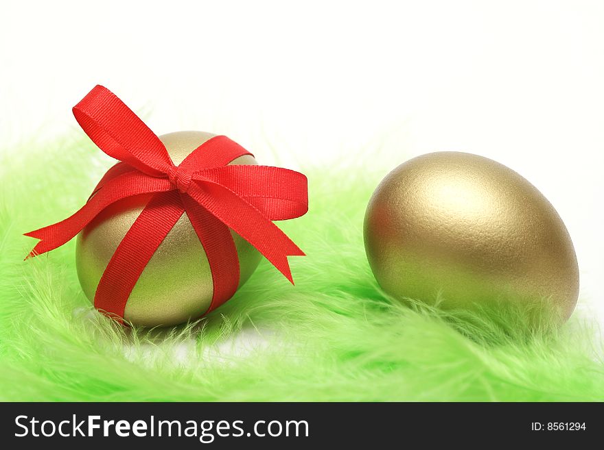 Golden egg wrapped around with red ribbon on green feathers. Golden egg wrapped around with red ribbon on green feathers