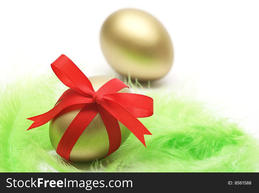 Golden egg wrapped around with red ribbon on green feathers. Golden egg wrapped around with red ribbon on green feathers