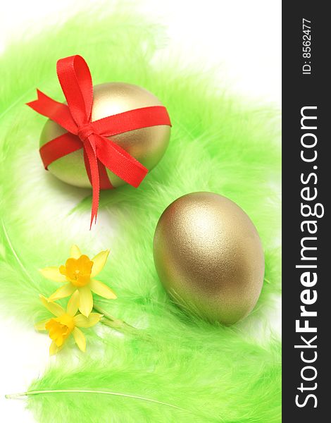 Golden easter eggs with yellow flowers and green feathers for easter background.