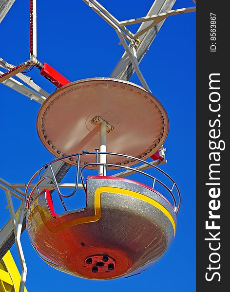 Funfair ferris wheel box and its suspension bracket over blue summer sky. Funfair ferris wheel box and its suspension bracket over blue summer sky.