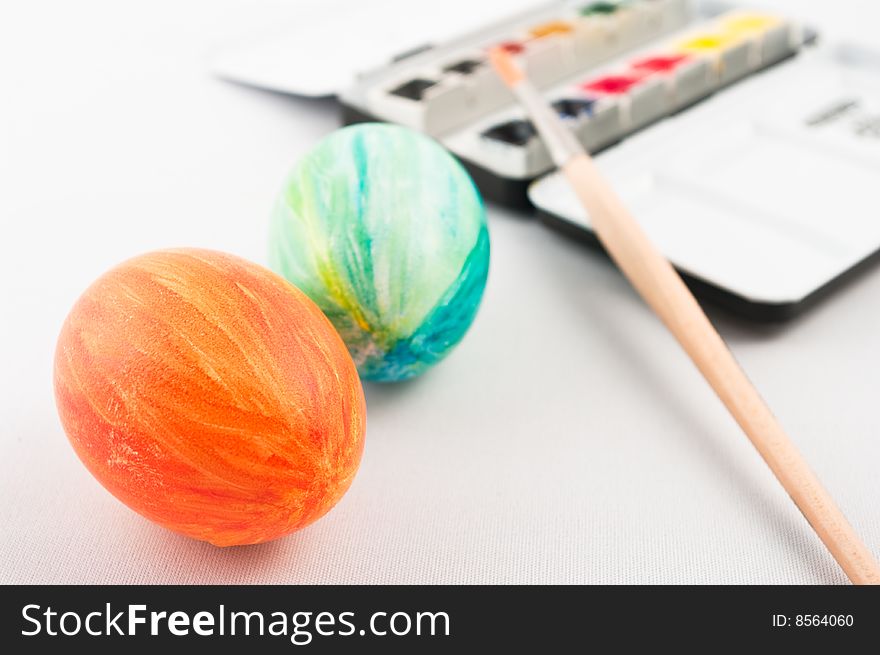 Two fresh painted easter eggs with brush and watercolor palette in background. Two fresh painted easter eggs with brush and watercolor palette in background.