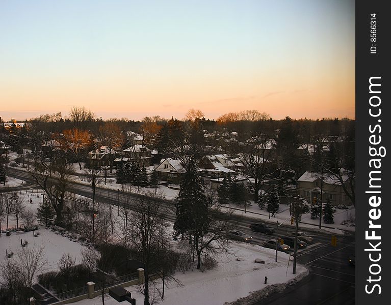 High angle shot on intersection at sunset with snow-covered roofs of houses and glowing trees. High angle shot on intersection at sunset with snow-covered roofs of houses and glowing trees.