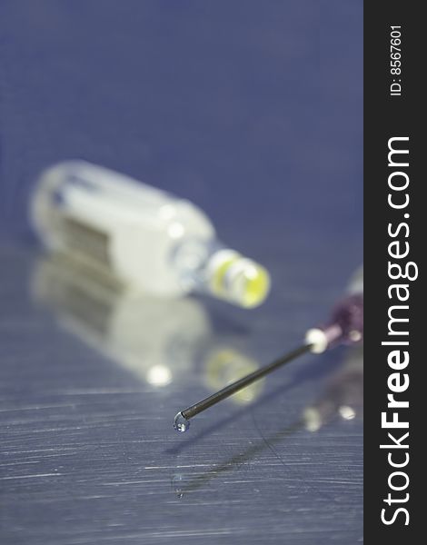 Syringe with sharp needle and droplet in shallow dof with ampule in background. Syringe with sharp needle and droplet in shallow dof with ampule in background