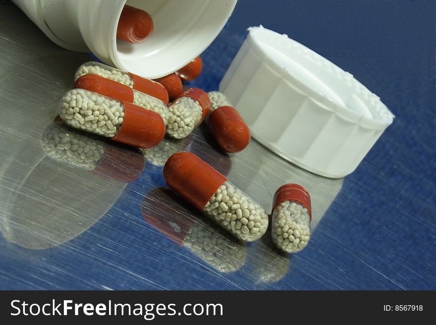 Red, brown capsules spilled on metal table with mirror effect on blue background. Red, brown capsules spilled on metal table with mirror effect on blue background