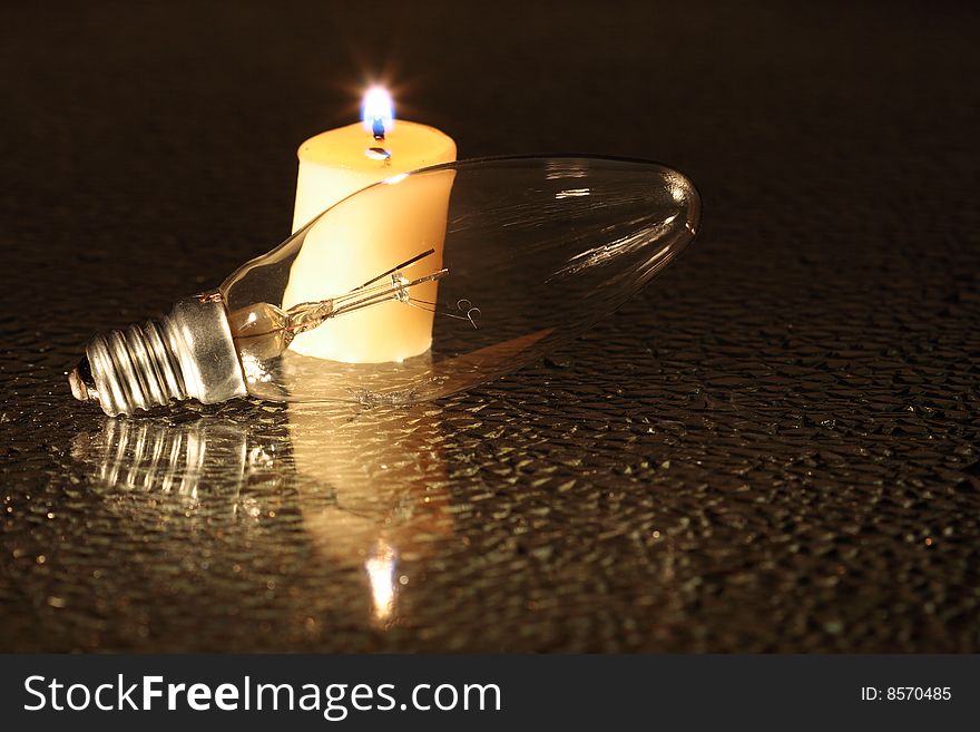 Burned-out bulb lying near burning candle on dark background. Burned-out bulb lying near burning candle on dark background