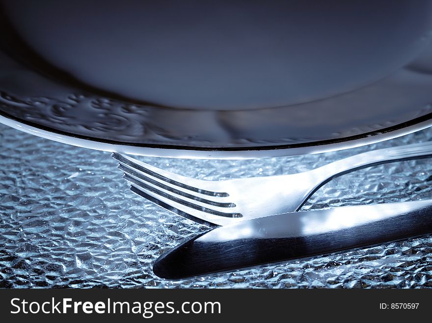 Fork and knife lying near plate on nice glassy background. Fork and knife lying near plate on nice glassy background