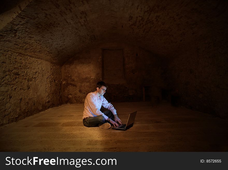 A man using a laptop in a cellar. A man using a laptop in a cellar