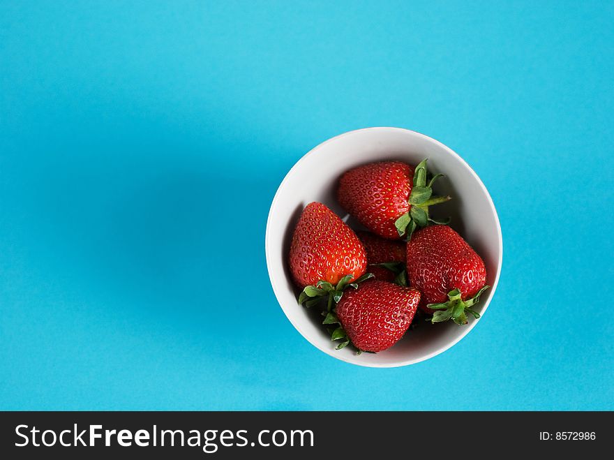 Bowl of strawberries on clear blue background