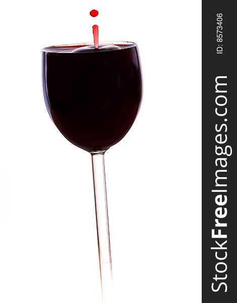 A drop of red wine falls into the glass isolated on white background