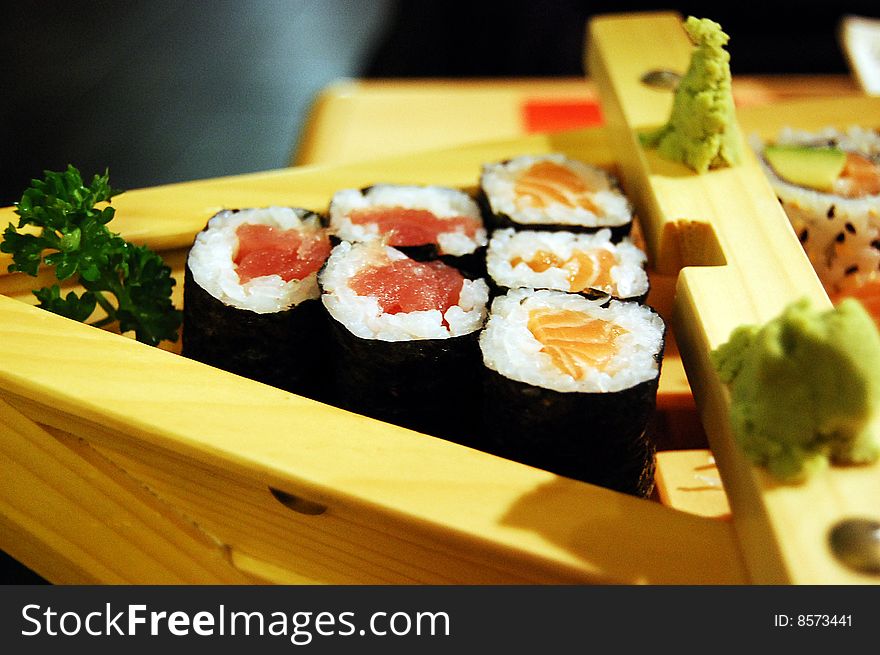 Small wooden boat-shaped plate with sushi: maki with salmon and tuna and some wasabi paste. Small wooden boat-shaped plate with sushi: maki with salmon and tuna and some wasabi paste