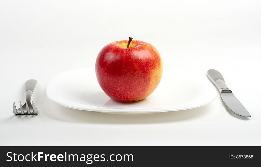 Fork, knife and red apple on white plate. Fork, knife and red apple on white plate