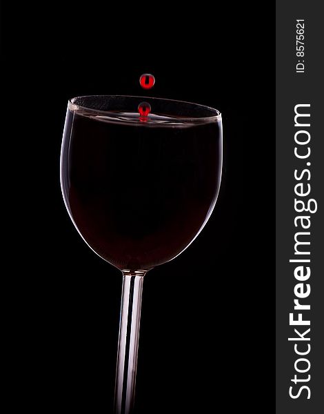 A drop of red wine falls into the glass isolated on black background