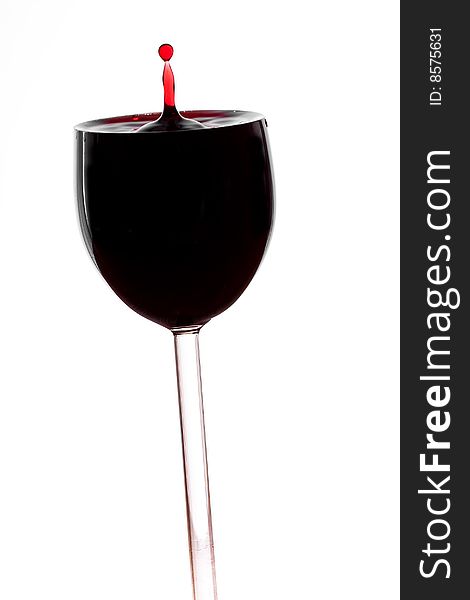 A drop of red wine falls into the glass isolated on white background