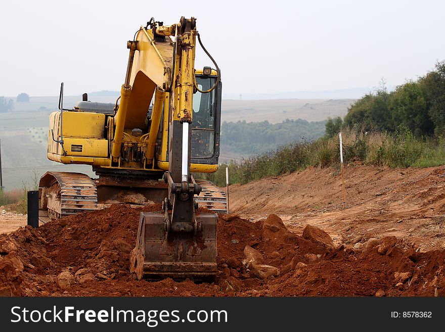 Partial side view of an excavator scooping up ground and rocks from a construction area. Partial side view of an excavator scooping up ground and rocks from a construction area