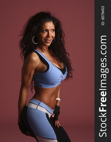 A fitness model with long flowing hair in studio wearing a blue, white, and black workout outfit with gloves and ear rings. A fitness model with long flowing hair in studio wearing a blue, white, and black workout outfit with gloves and ear rings.