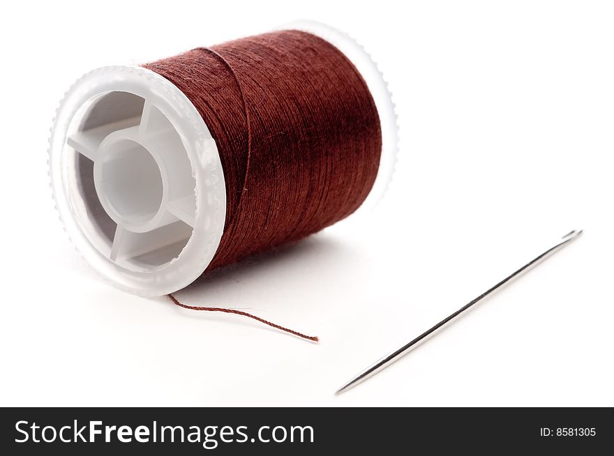 Horizontal extreme closeup of a spool of brown thread and a needle