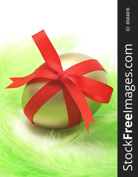 Golden egg wrapped around with red ribbon on green feathers.