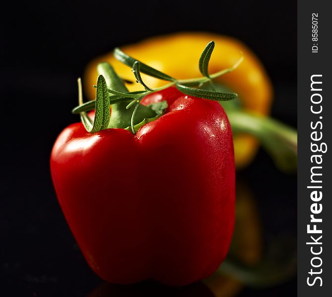 Red and yellow paprika with rosemary over black background. Red and yellow paprika with rosemary over black background