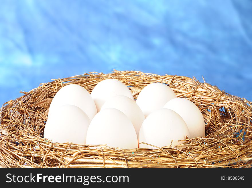 White eggs in golden nest on blue background