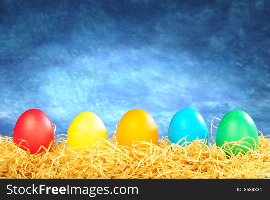 Five painted eggs on a straw on a blue background