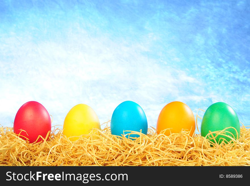 Five painted eggs on a straw on a clear sky background