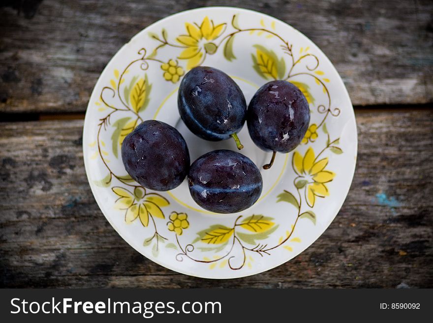 Four plums set on a plate with a flower pattern