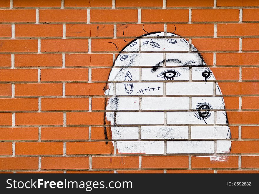 A brickwall with a graffiti showing an ugly white face. A brickwall with a graffiti showing an ugly white face