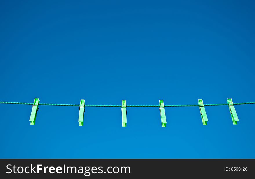 Green clothes pegs on a washing line against a blue sky background.