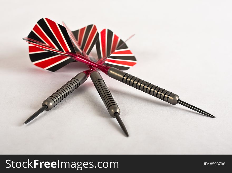 A set of 3 playing darts with red white and black plastic feathers and polished steel shafts.