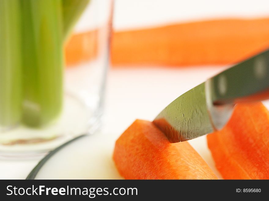 Close up of knife cutting a carrot with celery and more carrot on background. Close up of knife cutting a carrot with celery and more carrot on background