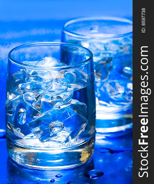 Glass with water and ice over blue