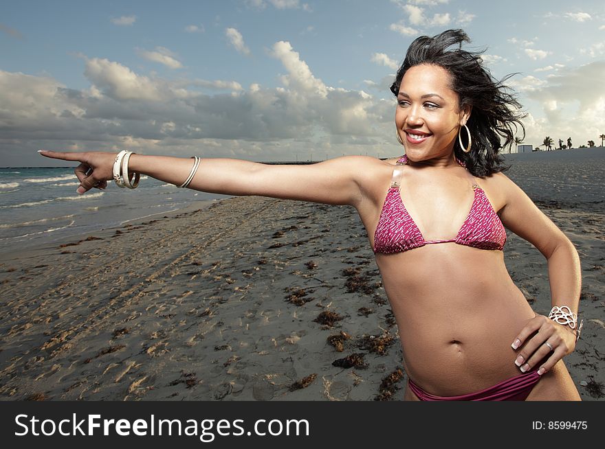 Young woman on the beach smiling and pointing towards the ocean