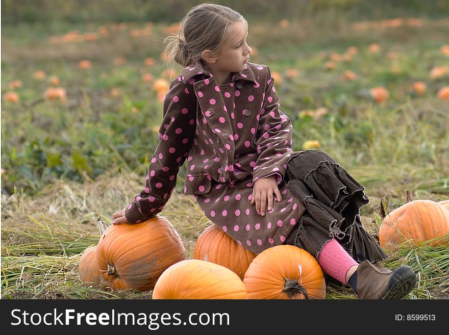 A pretty child dressed in a long polkadot coat and long skirt sits on a pumpkin in the middle of a field of pumpkins on a cold autumn day in rural Vermont. A pretty child dressed in a long polkadot coat and long skirt sits on a pumpkin in the middle of a field of pumpkins on a cold autumn day in rural Vermont